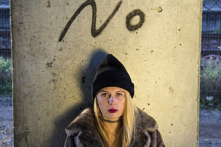 Eine junge Frau, die vor einem Betonpfeiler mit der Aufschrift „No” sitzt